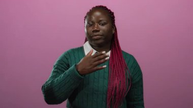 Göğsünde el olan Afrikalı Amerikalı kadın, izole edilmiş pembe arka plana karşı yemin ediyor. Samimiyet ve bağlılık ifade ediyor..