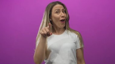 Beyaz tişörtlü orta yaşlı sarışın kadın pembe stüdyoda parmak işareti yapıyor, neşeli pozitiflik..