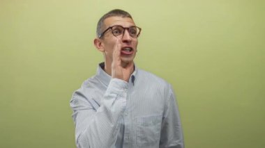 Gözlüklü beyaz adam, sarı duvara karşı neşeli bir ifadeyle konuşurken el kol hareketi yapıyor..