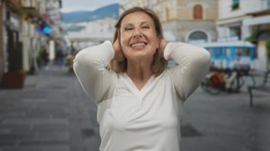 Kadın, bisiklet ve açık hava kafeleri ile kaplı hareketli şehir caddesinde iki eliyle boynuna dokunuyor..