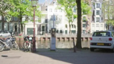 Hollanda 'da güneşli bir günde, odağını kaybetmiş bisiklet ve araba manzaralı manzaralı bir kanalın yanından geçen kadınlar..