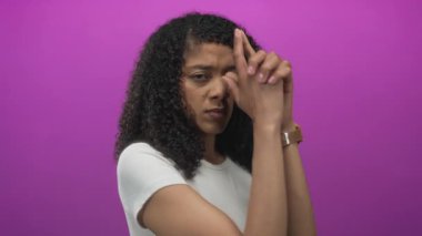 Afrikalı Amerikalı bir kadın mor bir stüdyoda kameraya parmak tabancası hareketi yapıyor..