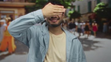 Genç adam gülümserken hareketli sokakta elleri ile gözlerini kapar; gizemli oyun merak mahremiyet.