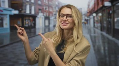 Şehrin caddesinde gülümseyen ve işaret eden bir kadın bulutlu hava altında bulanık binalarla şehir ortamını gösteriyor.