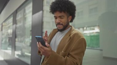 Şehirdeki Afro-Amerikan adam neşeli ifadeli akıllı telefon kullanıyor, şehir dışı yaşam tarzını ve teknolojik bağlantılarını gözler önüne seriyor.