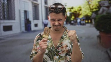 Açık şehir caddesinde dondurmalı, çiçekli gömlek ve güneş gözlüklü genç İspanyol adam güneşli bir günde canlı şehir ortamında turistik deneyimin tadını çıkarıyor.