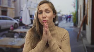 Açık hava restoranındaki bir kadın umut ve dua ifadesiyle aydınlık bir günde canlı bir şehir zeminiyle çevrili..