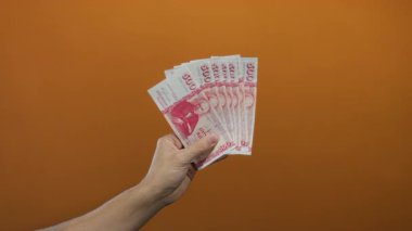 Kafkasyalı bir adam elinde turuncu arka plan duvarına karşı İzlanda Krona banknotları tutuyor, sermaye ve zenginlik kavramını sergiliyor..