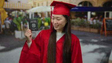 Kırmızı mezuniyet elbisesi giyen, elinde İtalyan pasaportu olan bir kadın şehrin caddesindeki kafe terasında kültürler arası başarı sergiliyor.