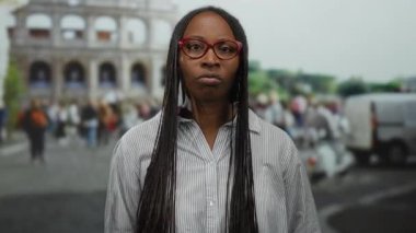 Roma 'da Roma Kolezyumu' nun yanında duran gözlüklü kadın açık havada hareketli bir ifadeyle tarihi mimari ve canlı şehir atmosferini gözler önüne seriyor..