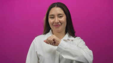 Beyaz gömlekli İspanyol kadın gülümseyerek yumruğunu kaldırıyor ve pembe duvarlı modern stüdyoya dik dik bakıyor..