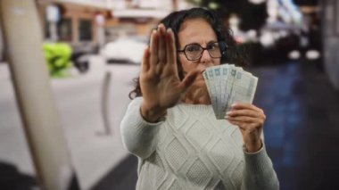 Bir şehir caddesinde elinde Mısır banknotları tutan orta yaşlı bir kadın. Durdurucu bir jestle açık hava ortamında finansal temalar gösteriyor..