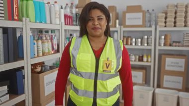 Yansıtıcı yelek giyen bir kadın, bağış malzemeleri ve kutuları ile çevrili bir hayır kurumunda destek veren gönüllü bir çevreye sahip olduğunu gösteren bağış merkezini onaylıyor..