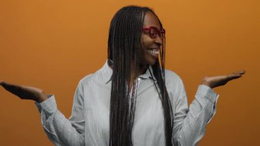 Kıvırcık saçlı, turuncu duvarın arkasında gülümseyen neşeli ve anlamlı pozlar veren bir kadın..