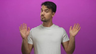 Hispanik bir adam canlı pembe bir arka plan önünde belirsizlik işareti yapıyor, beyaz bir gömlek giyiyor, kararsızlık ve kafa karışıklığını yansıtıyor..