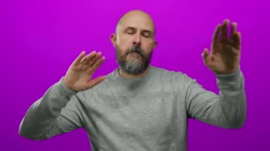 Gri kazaklı sakallı adam pembe arka planda dans figürleri sergiliyor..