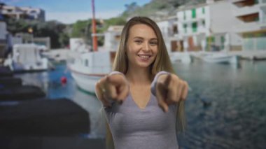 İskeleye yanaşmış teknelerle gülümseyen bir kadın, neşeli bir şekilde kameraya bakıyor açık gökyüzünün altında canlı, manzaralı bir yerde, neşeli bir ruh hali içinde..