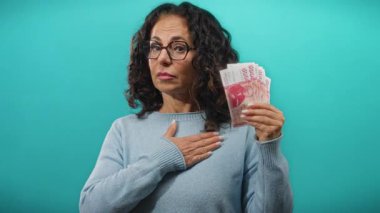 Orta yaşlı bir kadın, elinde İzlanda Krona banknotları tutarken mavi duvarlı arka planda el kaldırıyor..