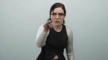 Gözlüklü esmer kadın, gri bir arka plana karşı kararlılıkla hareket ediyor. Güçlü duygularını ve özgüvenini vücut dili ve yüz ifadeleriyle ifade ediyor..