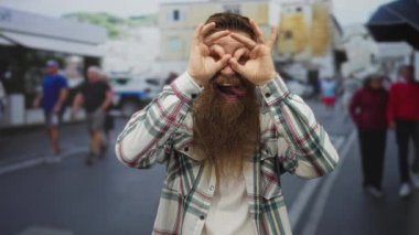 Uzun sakallı genç adam dürbünlü bir jest yapıyor..