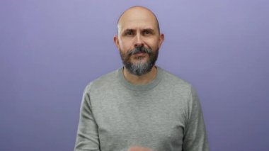 Sakallı yakışıklı kel adam, izole edilmiş mor arka plana karşı gizli bir jest yapar. Gizlilik ya da gizemi ifade eden yüzü ve ince el hareketiyle aktarır..