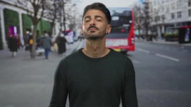 Bulanık kalabalıklar ve yüksek binalar arasında kalabalık şehir caddesinde kırmızı otobüsü işaret eden adam, kendine güvenen farkındalık.