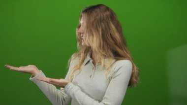 Stüdyo vitrinlerinde el falı olan kadın genç sarışın görünümlü ve yeşil arka planda süveter giyerken gülümseyen..