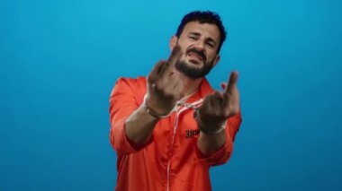 Elleri kelepçeli, turuncu hapishane tulumlu İspanyol bir adam mavi arka planda dramatik bir hapis ve meydan okuma sahnesi anlatıyor..