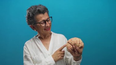 Gözlüklü, gülümseyen ve parlak mavi bir arkaplan karşısında beyin modelini gösteren son sınıf öğrencisi kadın eğitim ve bilgelik temalarını aktarıyor..