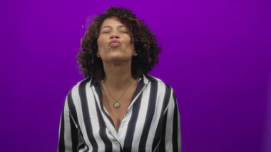 Kadın dudakları üfleme jesti siyah beyaz çizgili gömlek canlı mor stüdyo arka planı karşı; neşeli neşe.