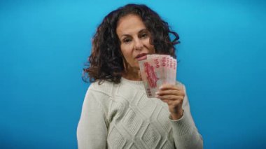 Elinde mavi bir duvara karşı Tayvan banknotları tutan, el kol hareketi yapan, para ve finans kavramlarını taşıyan orta yaşlı, izole bir ortamda ele geçirilen bir kadın..