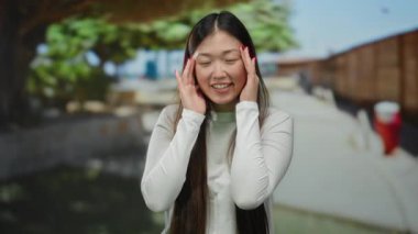 Güneşli bir şehir caddesinde gülümseyen bir kadın neşeli bir ifadeyle ve şık uzun saçlarıyla açık havada enerjik bir hava sergiliyor..