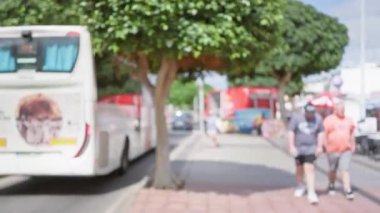 Ianzarote 'de açık hava manzarası bulanık. Güneşli bir günde odandan çıkmış insanlar ve otobüsler ağaçların altında.