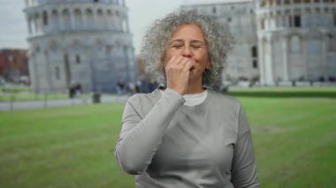 Gri saçlı bir kadın sidik kulesinin önünde gülümsüyor, İtalya, günlük gri kıyafetler giyiyor, ikonik şehirde kültürel atmosferi yakalıyor..