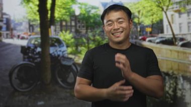 Genç Çinli bir adam güneşli bir caddede park halindeki bisikletin yanında el ile yanağa dokunur; memnuniyet.