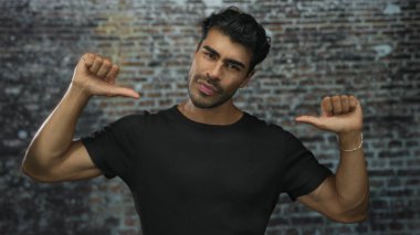 Siyah tişörtlü genç İspanyol bir adam stüdyoda duvara başparmak işareti yapıyor..