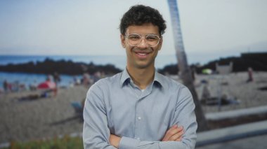 Güneşli yaz sahillerinde kolları çapraz duran gözlüklü bir adam arkasında insanlar, özgüven..