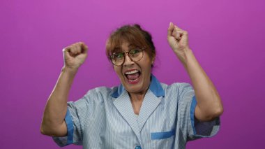 Kıdemli İspanyol kadın üniformalı temizlikçi neşeli bir şekilde canlı pembe bir duvara karşı kutluyor izole edilmiş arka plan mutluluk ve enerji gösteriyor..