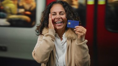 Tren istasyonunda elinde mavi kredi kartıyla gülümseyen bir kadın bulanık bir tren geçmişine karşı duygu ve modern şehir yaşam tarzını yakalıyor..