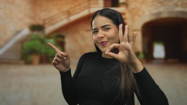 Manzaralı arka planı olan eski bir kasabada mutlu bir şekilde el kol hareketi yapan kadın, pozitiflik ve neşe ifade ediyor, şehir dışında gezmek ve kültürel temalar için ideal..