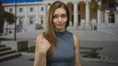 Parlak güneş ışığı altında sütunları olan neoklasik bir binanın yakınındaki boş sokağa başparmağını gösteren kadın; kayıtsızlık.