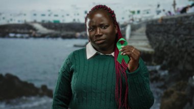 Deniz kenarında elinde yeşil kurdele tutan bir kadın okyanus zeminiyle doğanın farkındalığını ve bağlantısını temsil ediyor.