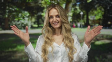Güneşli bir park ortamında neşeli bir şekilde gülümseyen kadın, yemyeşil ağaçlarla çevrili, huzurlu bir açık havada mutluluk ve sükunet yayıyor..