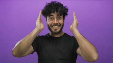 Sakallı genç İspanyol bir adam, parlak mor bir arka plana karşı elleriyle yüzünü örtüp açarken ciddi ve gülümseyen yüz ifadeleri arasında gidip geliyor..