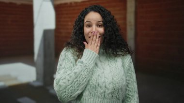 Bir inşaat alanında kapalı alanda gülümseyen süveter giyen genç İspanyol kadın neşeli bir ifade ve rahat bir tavır sergiliyor..