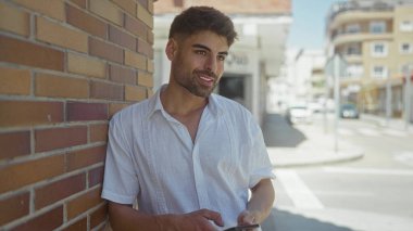 Tuğladan duvara yaslanmış beyaz gömlekli, açık mavi gökyüzünün altında telefonla konuşan adam. Mutluluk..