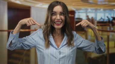 Otel binasında gülümseyen ve kendini gösteren gözlüklü genç bir kadın..