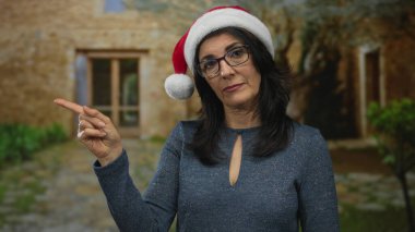 Noel Baba şapkası takan İspanyol kadın bina girişinde izleyiciye işaret ediyor; reddedilme.