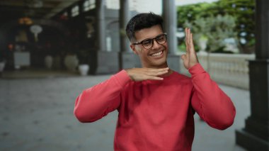 Yakışıklı, açık havada gülümseyen, gözlüklü, açık havada kırmızı kazak giyen çekici, şehir çocuğu, sokak fotoğrafı çeken, mutlu, rahat, yetişkin erkek.