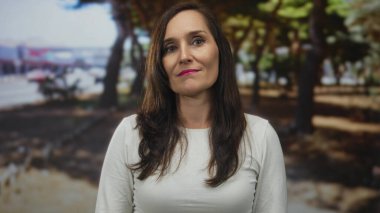 Yeşil bir park ortamında kendine güvenen bir kadın doğal güzelliğini ve zarafetini sergiliyor. Etrafı yemyeşil ağaçlarla çevrili..